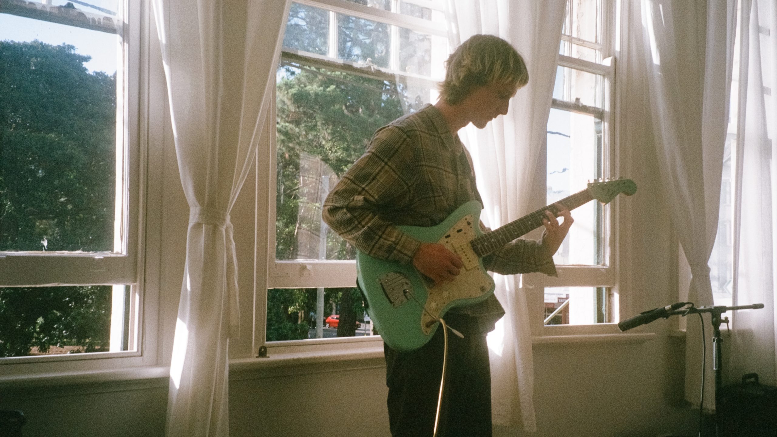 Musician Bluetung stands in a sunlit room, playing guitar